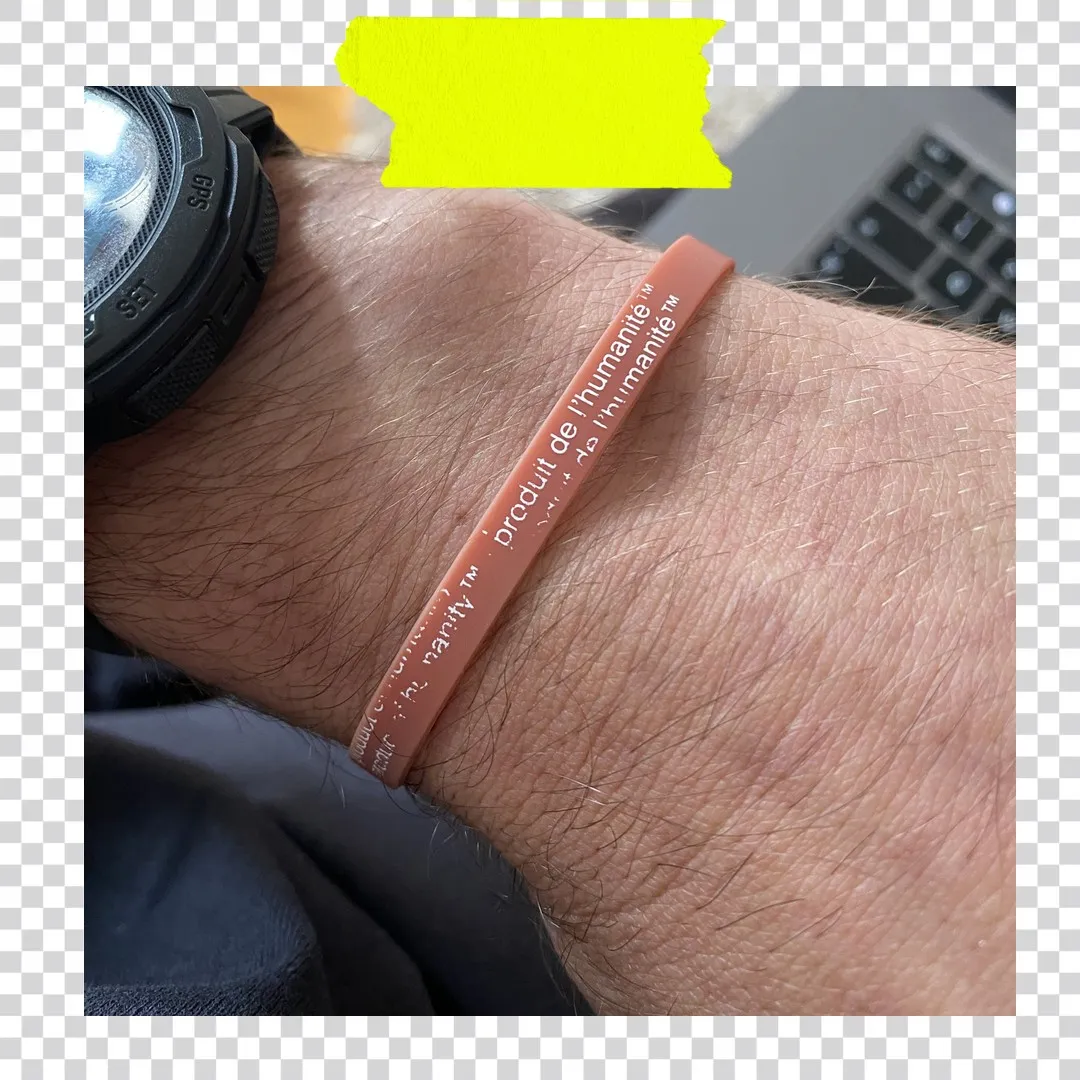 Rosa Silikonarmband mit weißem Aufdruck „product of humanity™“ und „produit de l’humanité™“ an einem Handgelenk