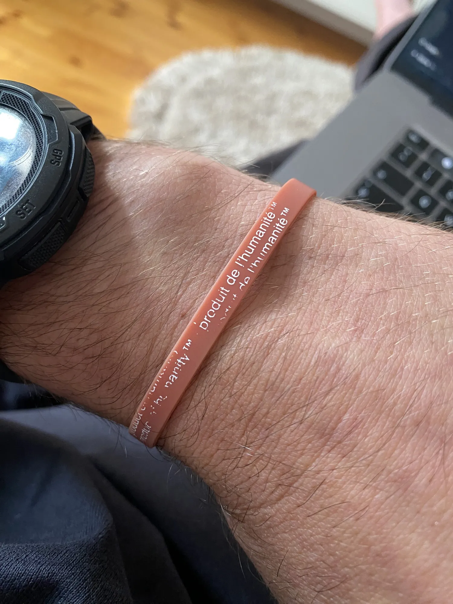 Rosa Silikonarmband mit weißem Aufdruck „product of humanity™“ und „produit de l’humanité™“ an einem Handgelenk