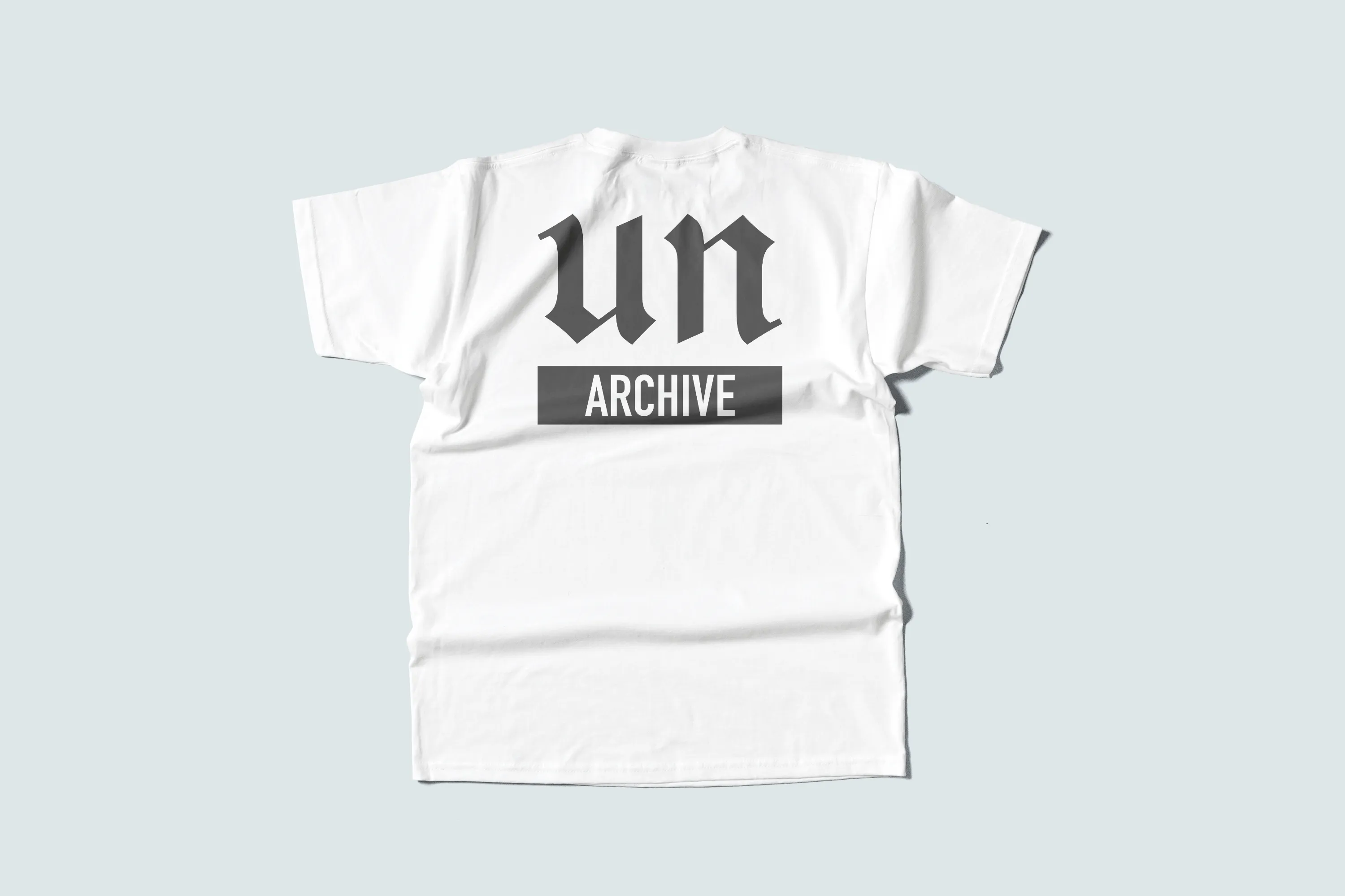 Weißes T-Shirt von hinten mit „un“ in gebrochener Schrift über einem grauen Balken mit „ARCHIVE“